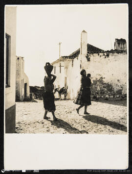 Mulher com cântaro de água à cabeça numa rua da pederneira